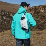 Sac Banane Trek Hydratation Roll-Top Sac banane blanc porté en bandoulière dans le dos par un homme lors d'une randonnée en montagne