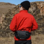 Sac Banane Trek Hydratation Roll-Top Sac banane noir porté à la taille dans le bas du dos par une femme lors d'une randonnée en montagne