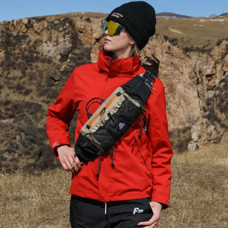 Sac banane beige et noir porté en bandoulière sur la poitrine par une femme en randonnée en montagne