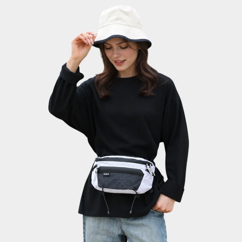 Sac banane ripstop blanc quadrillé porté à la taille par une femme de face avec poche avant en filet noir