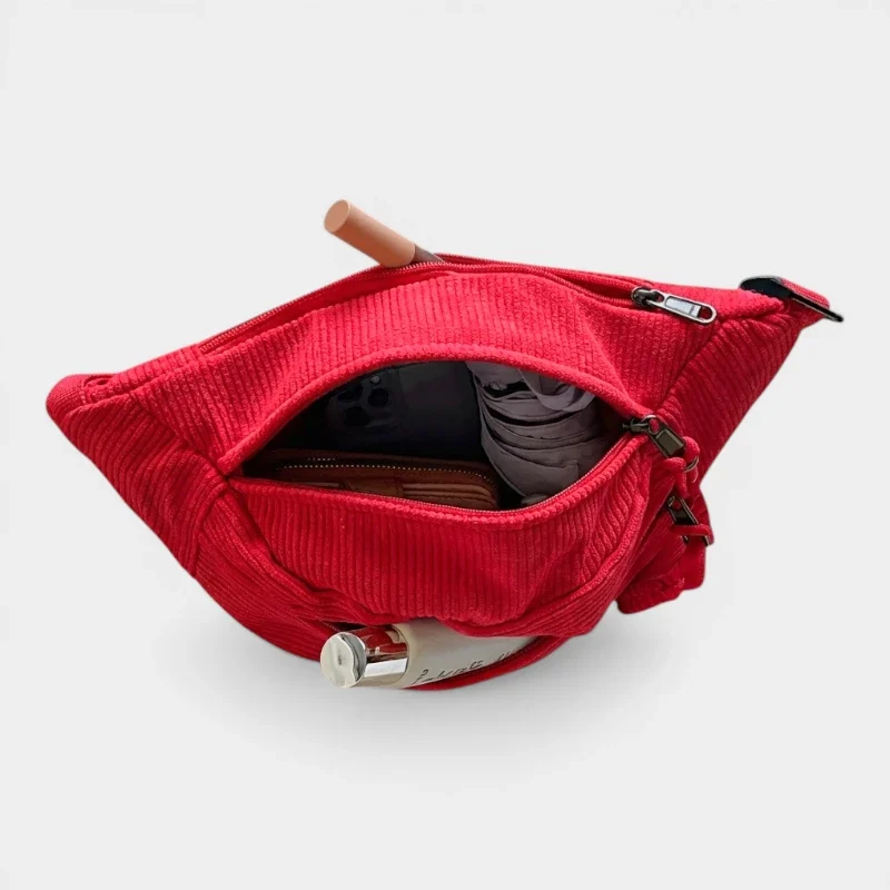 Banane en velours côtelé rouge vue de dessus, poche principale ouverte révélant divers essentiels à l'intérieur