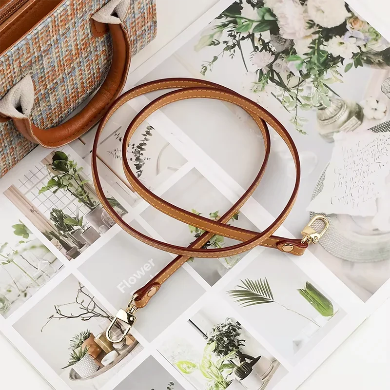 Bandoulière Cuir Fine marron aux coutures visibles avec mousquetons dorés posée près d’un sac classique