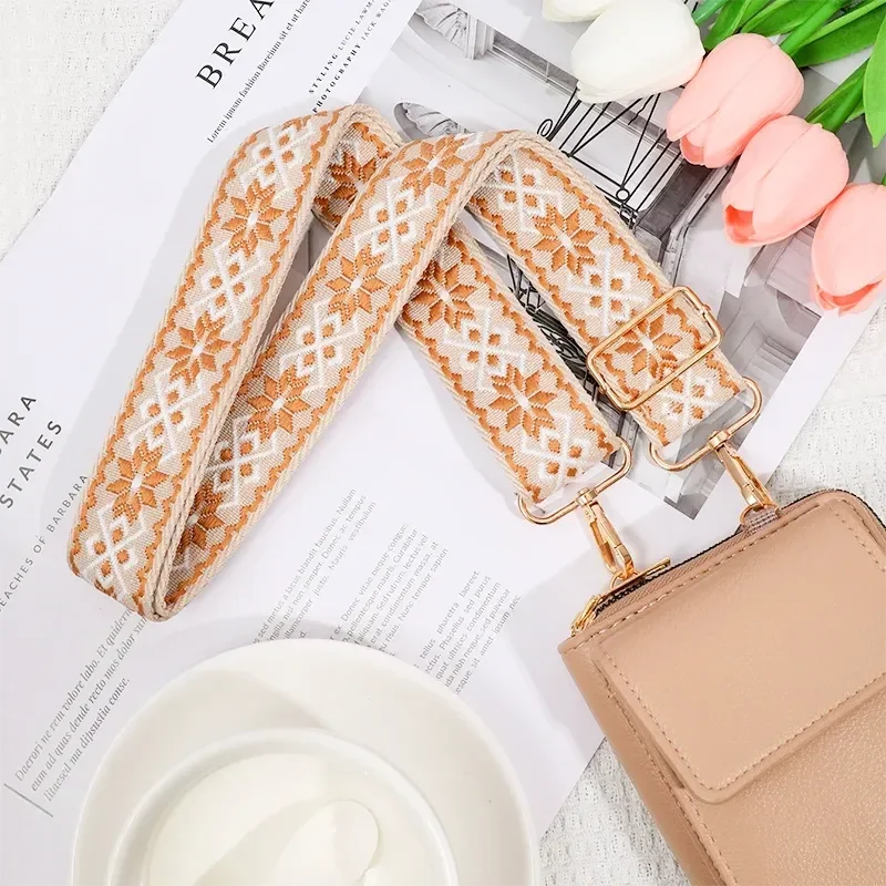 Bandoulière Motifs Jacquard Nordique beige avec motifs floraux et mousquetons dorés attachée à un sac clair.