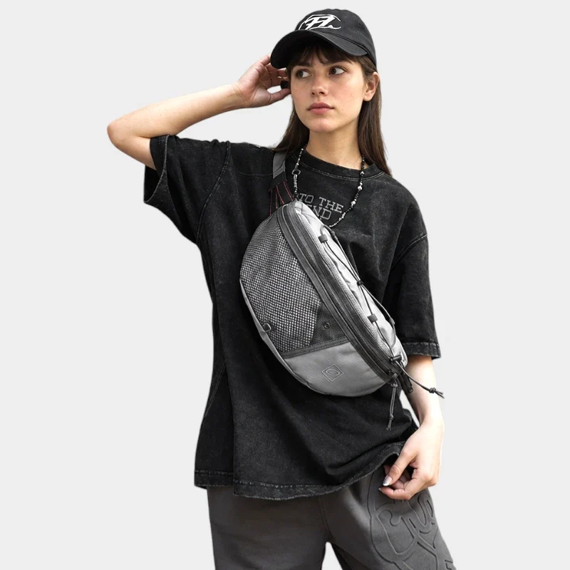 Sac banane gris porté en bandoulière sur le torse par une femme de face au style streetwear