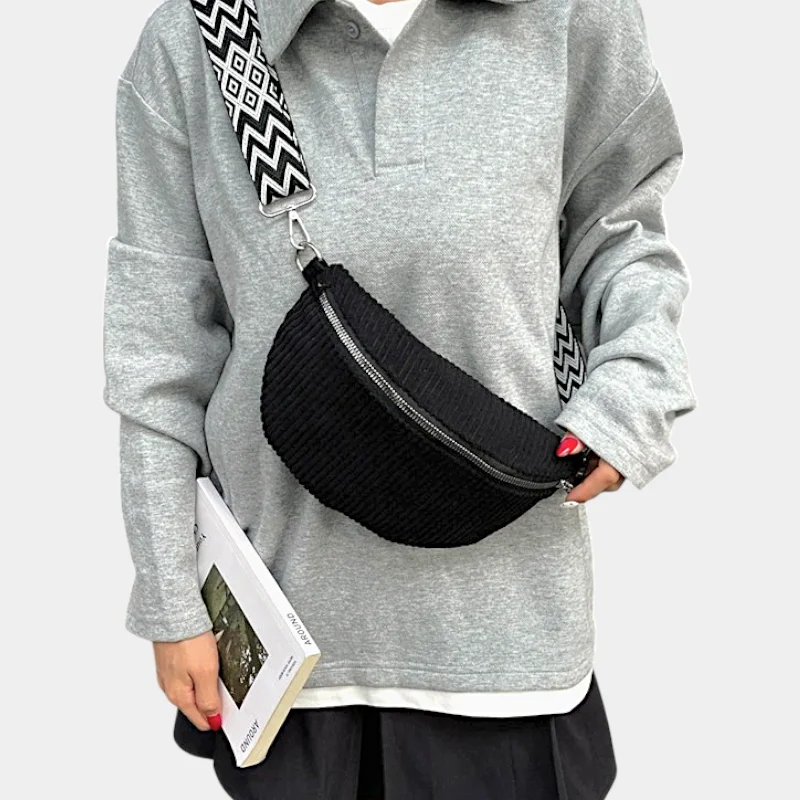 Petit Sac Banane Velours Côtelé Bandoulière Femme de couleur noire porté en travers du corps avec une lanière à motifs sur un pull gris