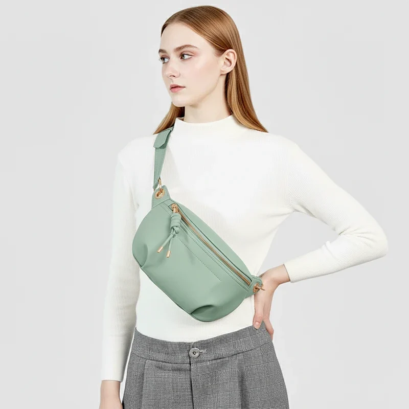 Sac Banane Cuir Coloré de couleur vert pâle porté en bandoulière par une femme avec un pull blanc et une jupe en plaid
