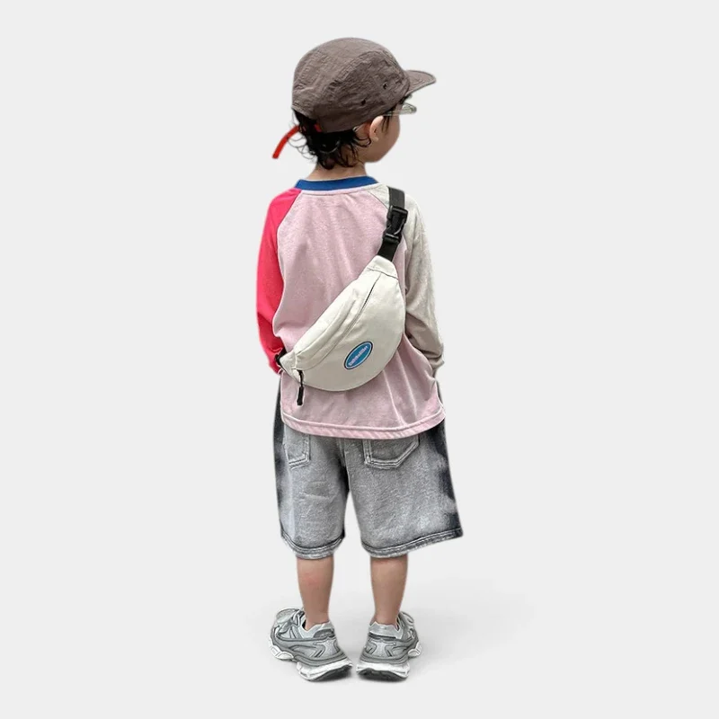 Sac banane enfant en toile de nylon blanc cassé porté en bandoulière dans le dos par un petit garçon vu de dos