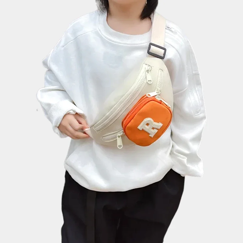 Sac banane enfant crème à poche avant orange porté en bandoulière sur la poitrine par un enfant