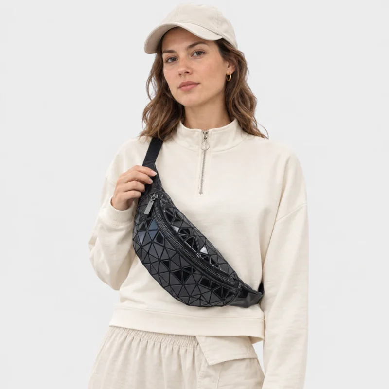 Sac banane en PVC noir brillant porté en bandoulière par une femme de face au style sportswear décontracté