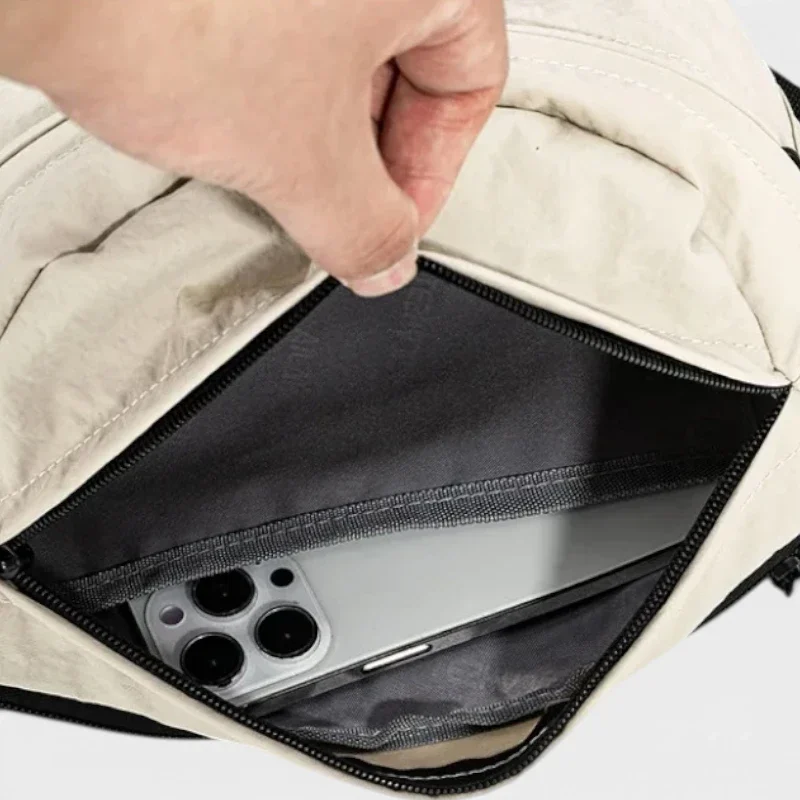 Sac banane nylon beige, gros plan sur la poche avant ouverte révélant un smartphone