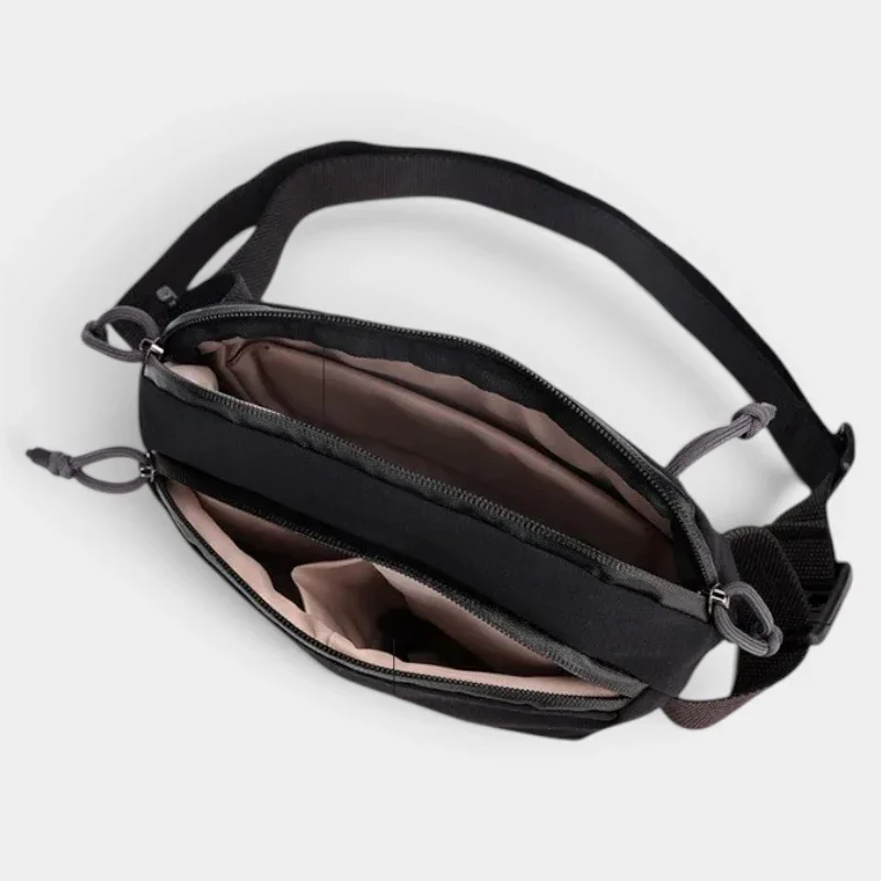Sac banane nylon noir au style gorpcore, vu de dessus avec la poche principale ouverte révélant des poches zippées intérieures