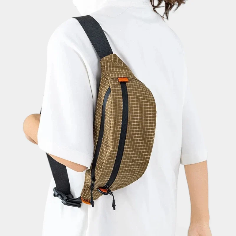 Sac banane nylon quadrillé marron clair porté en bandoulière de dos par une femme au style casual-chic