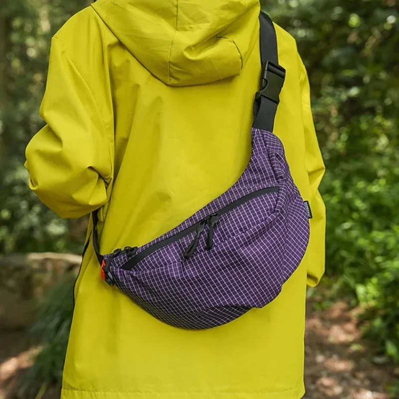 Sac banane nylon quadrillé violet porté en bandoulière dans le dos par une personne au style outdoor