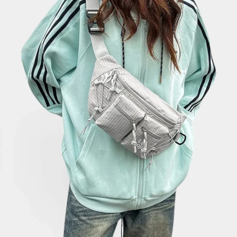Sac banane nylon gris clair porté en bandoulière croisée par une femme au style streetwear décontracté