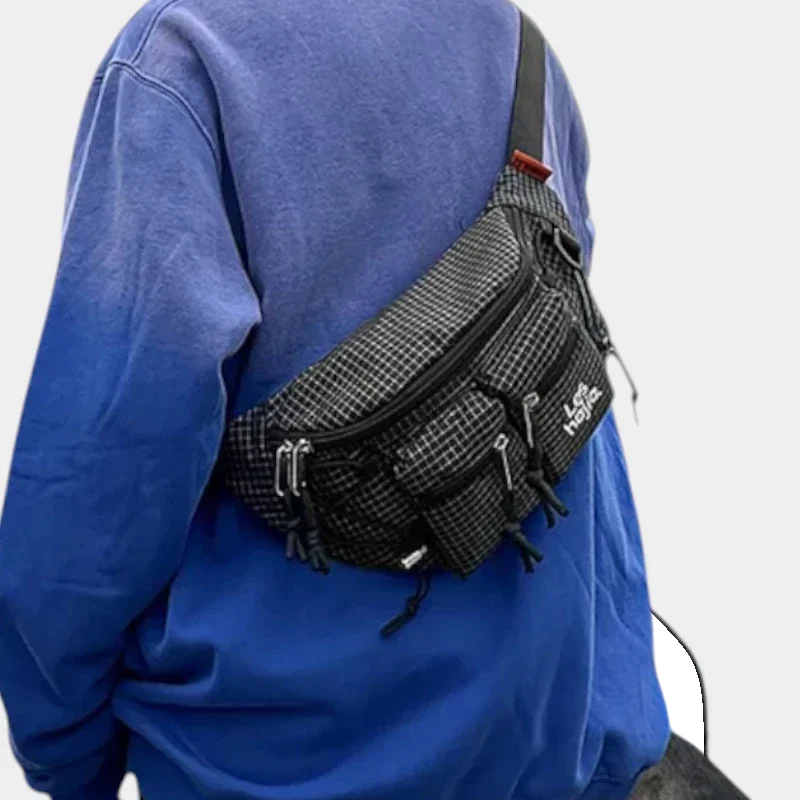Sac banane nylon à motif quadrillé noir et gris, porté en bandoulière dans le dos par une personne au style streetwear