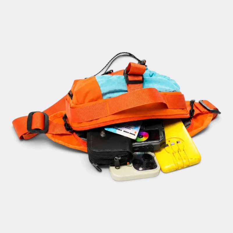 Sac banane orange vu de dessus avec sa poche principale ouverte sur un téléphone et un portefeuille