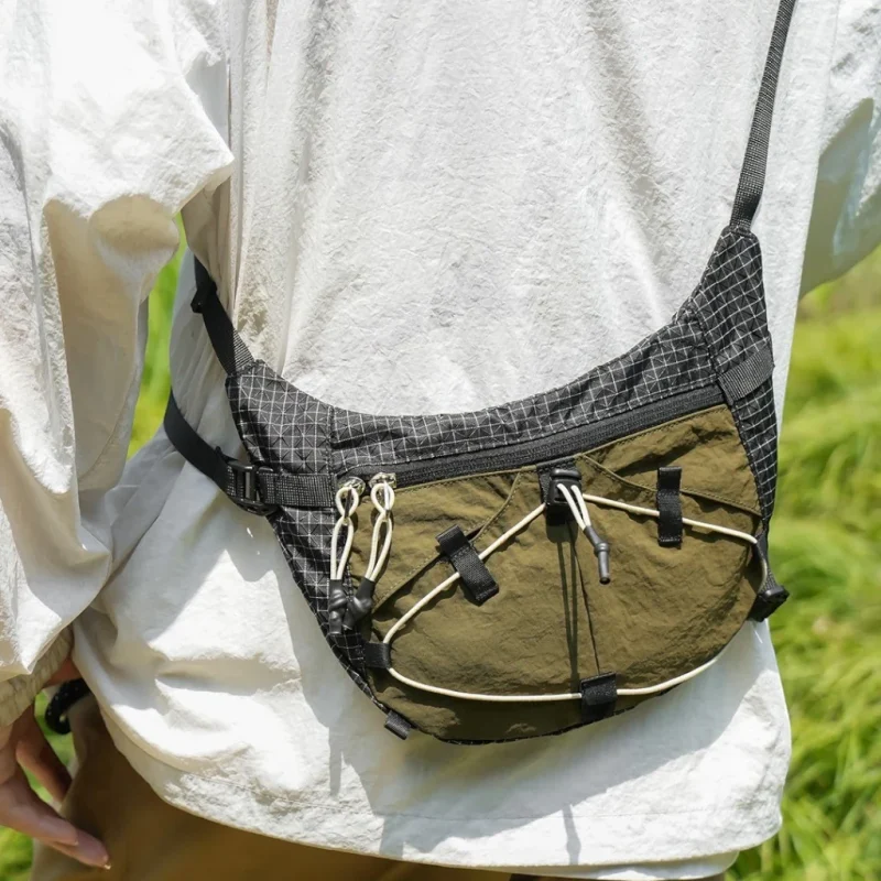 Sac banane noir et kaki porté en bandoulière vu de près avec cordon élastique écru et double tirette