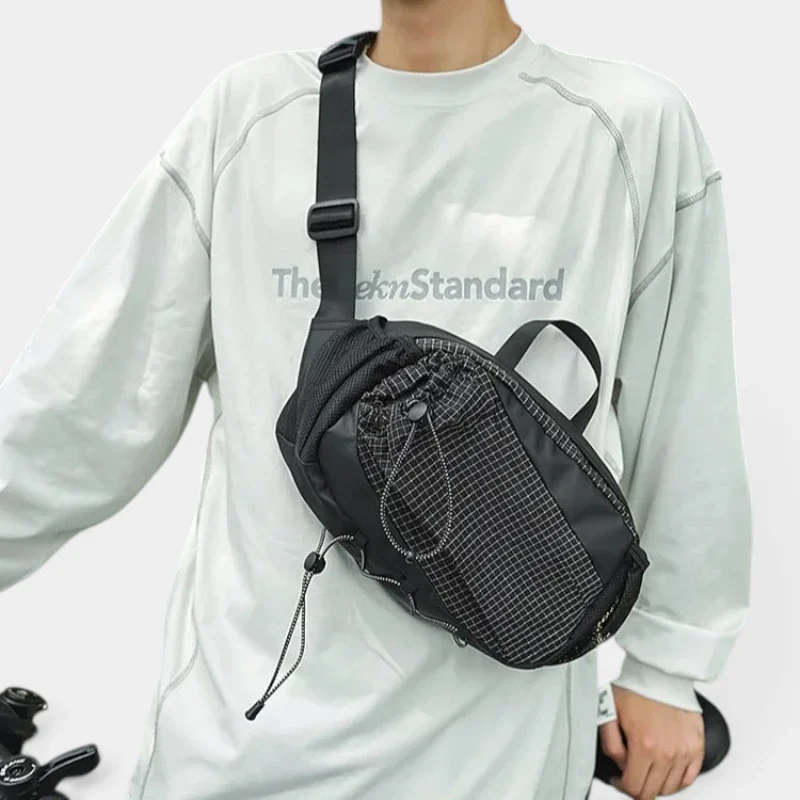 Grand sac banane randonnée en nylon noir porté en bandoulière par un homme au style streetwear