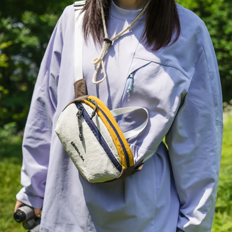Sac banane en nylon froissé blanc à bande jaune porté en bandoulière sur la poitrine par une femme