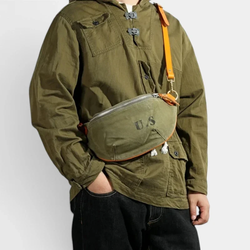 Sac banane toile kaki militaire porté en bandoulière par un homme au style workwear, avec sangle en cuir orange