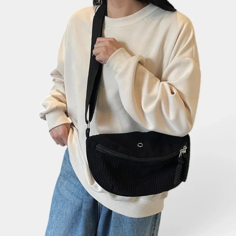 Sac banane velours côtelé demi-lune noir porté en bandoulière par une femme au style casual-chic