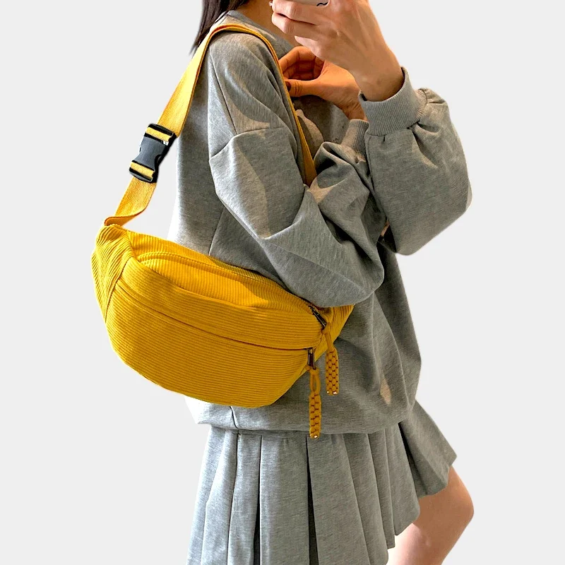 Sac banane velours côtelé jaune porté en bandoulière par une femme, avec sangle à motif rayé et boucle plastique