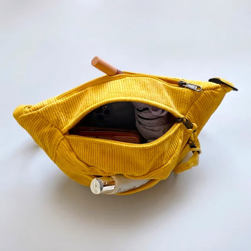 Sac banane velours côtelé jaune posé vu de dessus, poche principale ouverte avec essentiels visibles à l’intérieur