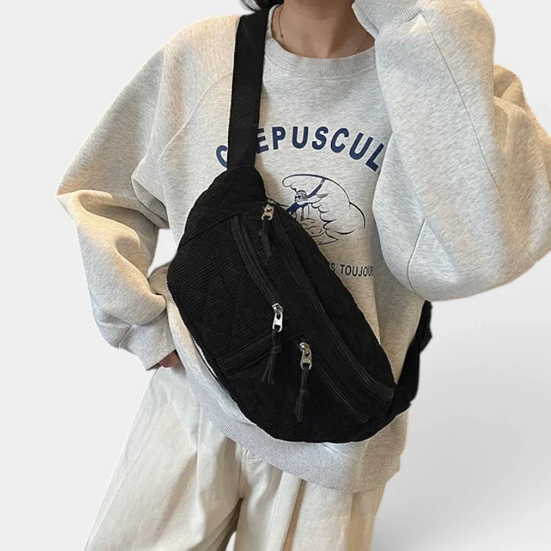 Sac banane en velours côtelé noir porté en bandoulière par une femme de face au style casual-sport