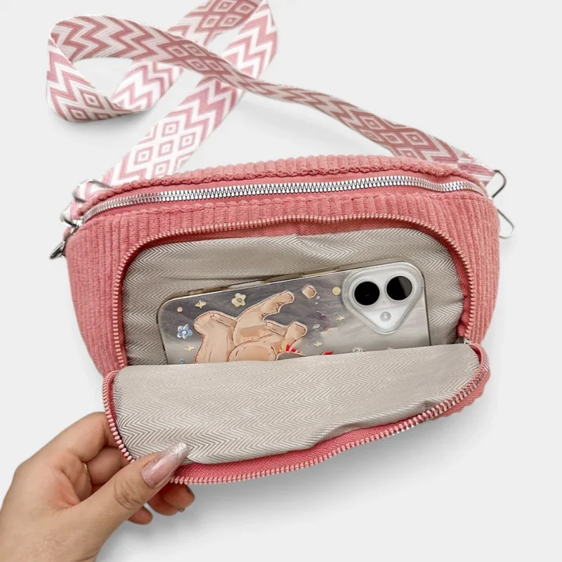 Sac banane velours côtelé rose présenté à plat vue de face, poche avant ouverte révélant une doublure chevronnée claire et un téléphone