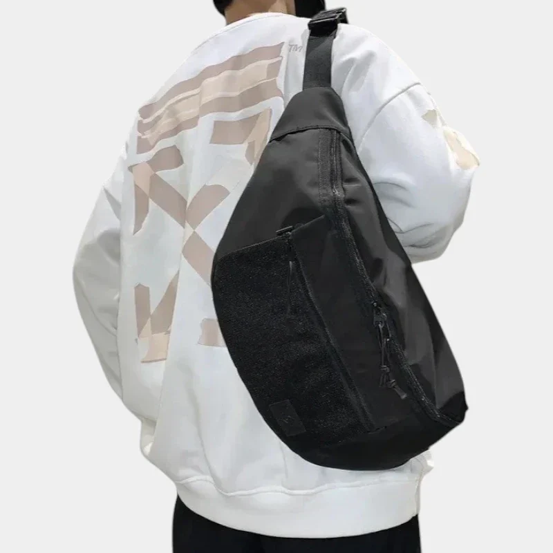 Grand sac banane XXL en nylon noir porté en bandoulière par un homme de dos au style streetwear